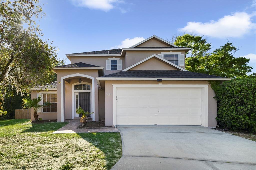 A two-story suburban house with a beige stucco exterior, a two-car garage, and arched entryway — 168 IMPERIAL OAK COURT, DAVENPORT, FL