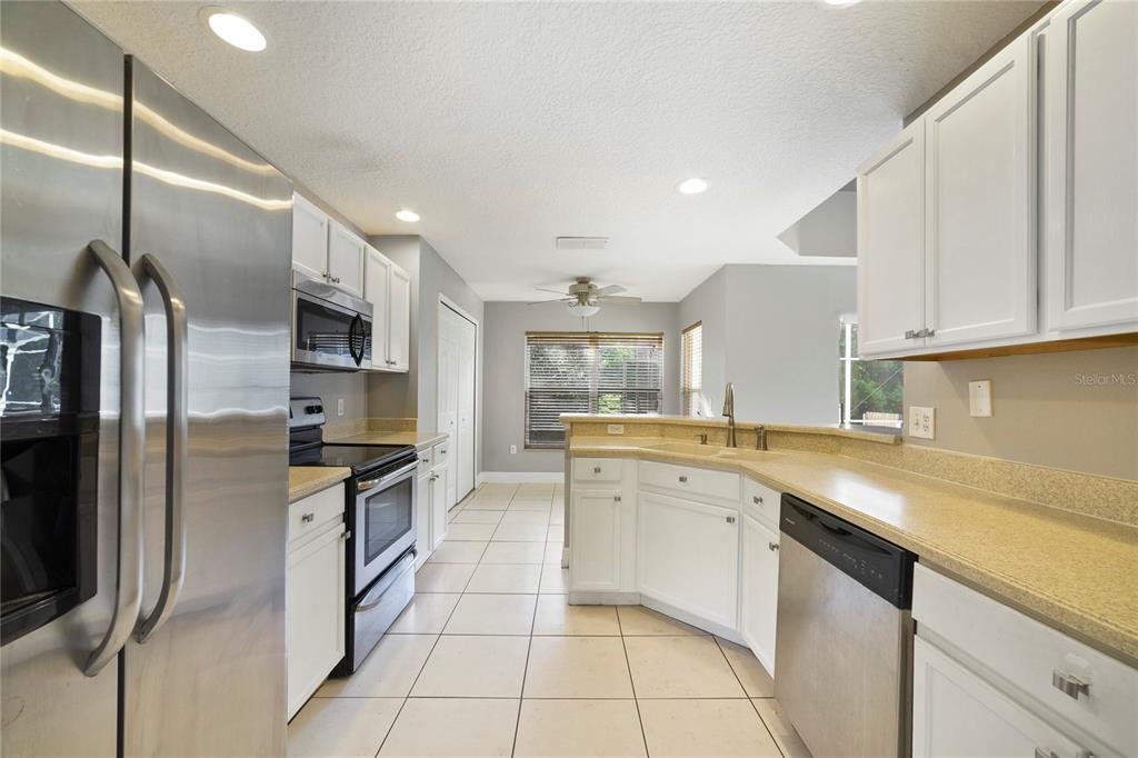 A kitchen features white cabinets, stainless steel appliances, tan countertops, and light tile flooring — 168 IMPERIAL OAK COURT, DAVENPORT, FL