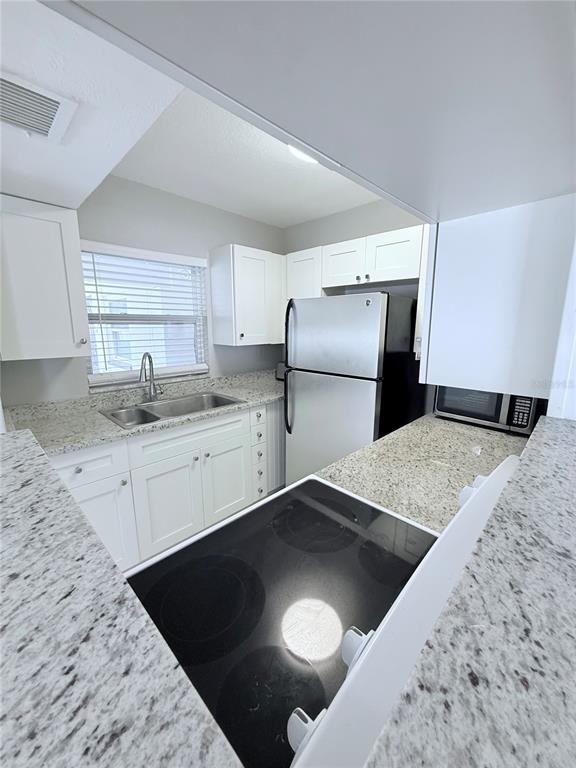 A kitchen features white cabinets, granite countertops, stainless steel appliances, and a glass-top stove — 11705 3RD STREET E UNIT 8, TREASURE ISLAND, FL