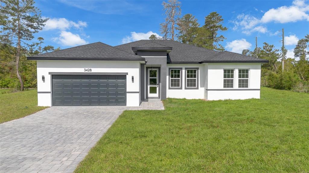A single-story house with white stucco walls, a dark gray roof, and a paved driveway — 3428 SW 165TH LOOP, OCALA, FL