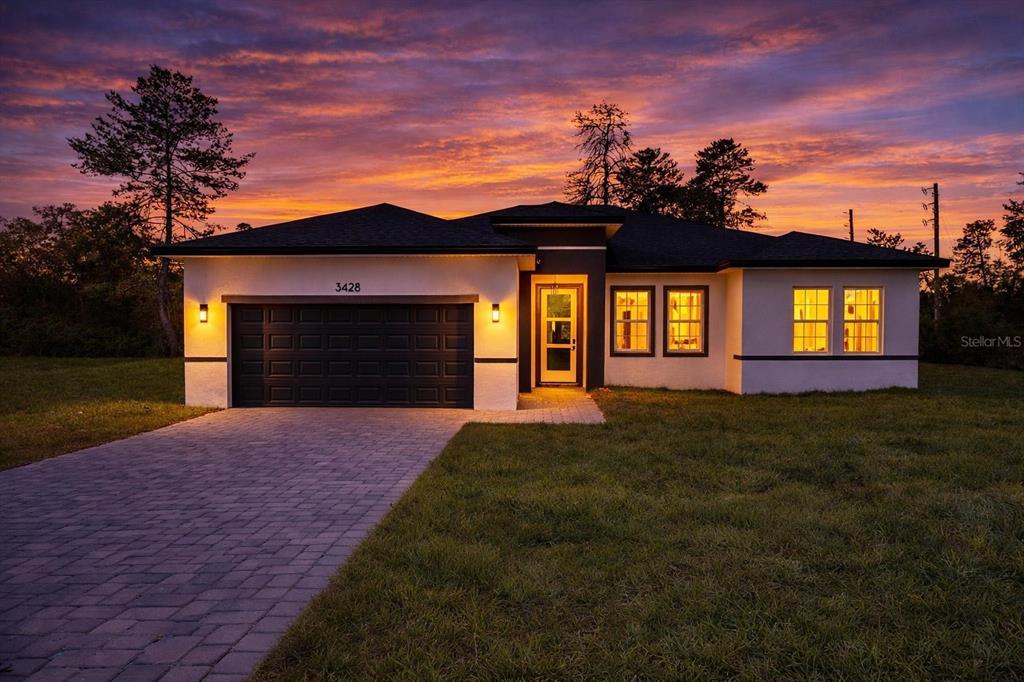 A single-story house with a dark garage door and white exterior at sunset — 3428 SW 165TH LOOP, OCALA, FL