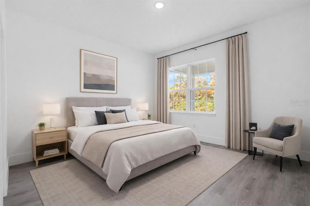A bedroom features a bed with neutral bedding, a nightstand, an armchair, and a window — 3428 SW 165TH LOOP, OCALA, FL