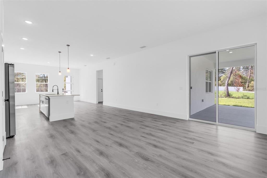 A bright, open-concept kitchen and living area features white walls, gray wood-look flooring, and sliding doors — 3428 SW 165TH LOOP, OCALA, FL