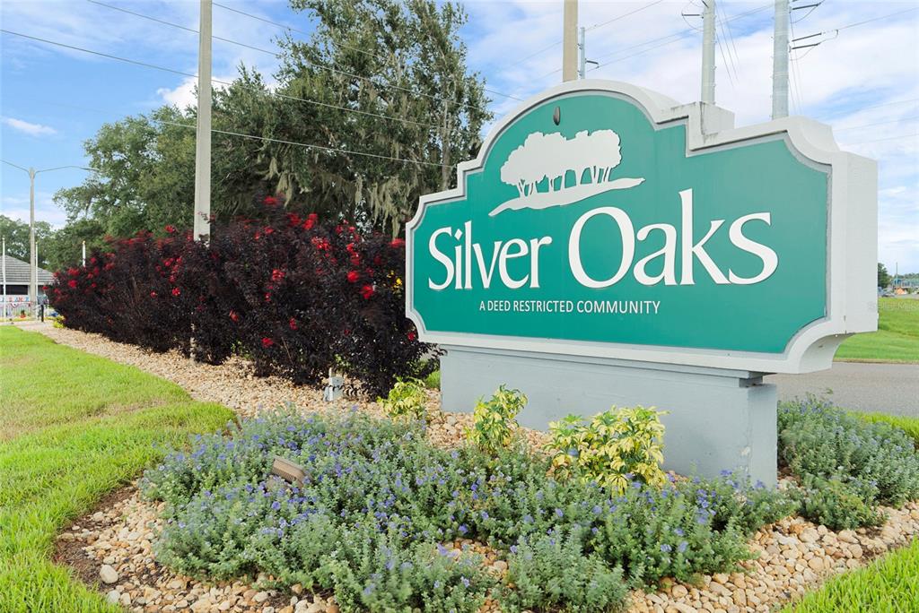 A teal community entrance sign for Silver Oaks stands in a landscaped garden bed — 6412 LAURELWOOD DRIVE, ZEPHYRHILLS, FL