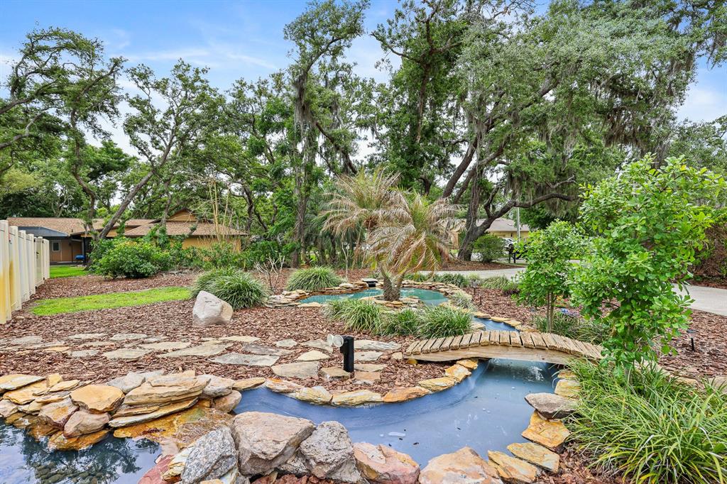 A backyard features a stone-lined pond with a small wooden bridge and lush landscaping — 2925 CHELSEA WOODS DRIVE, VALRICO, FL
