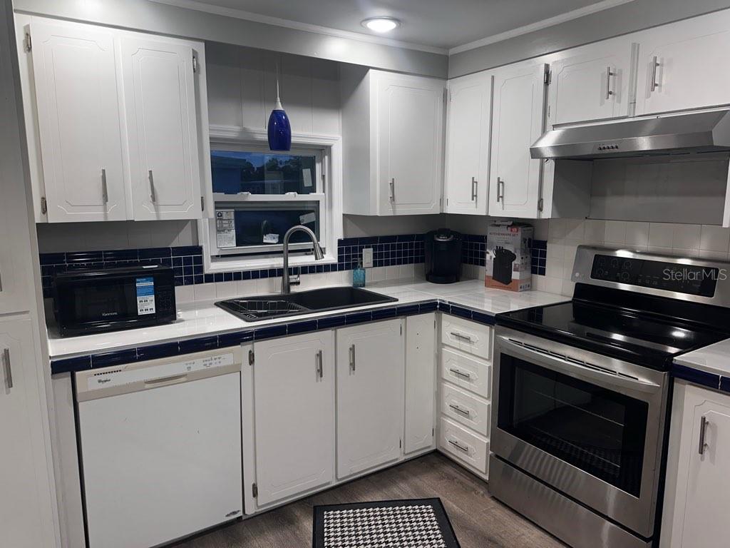 A kitchen features white cabinets, dark blue tiled countertops, and stainless steel appliances — 530 SUN UP STREET, NORTH FORT MYERS, FL