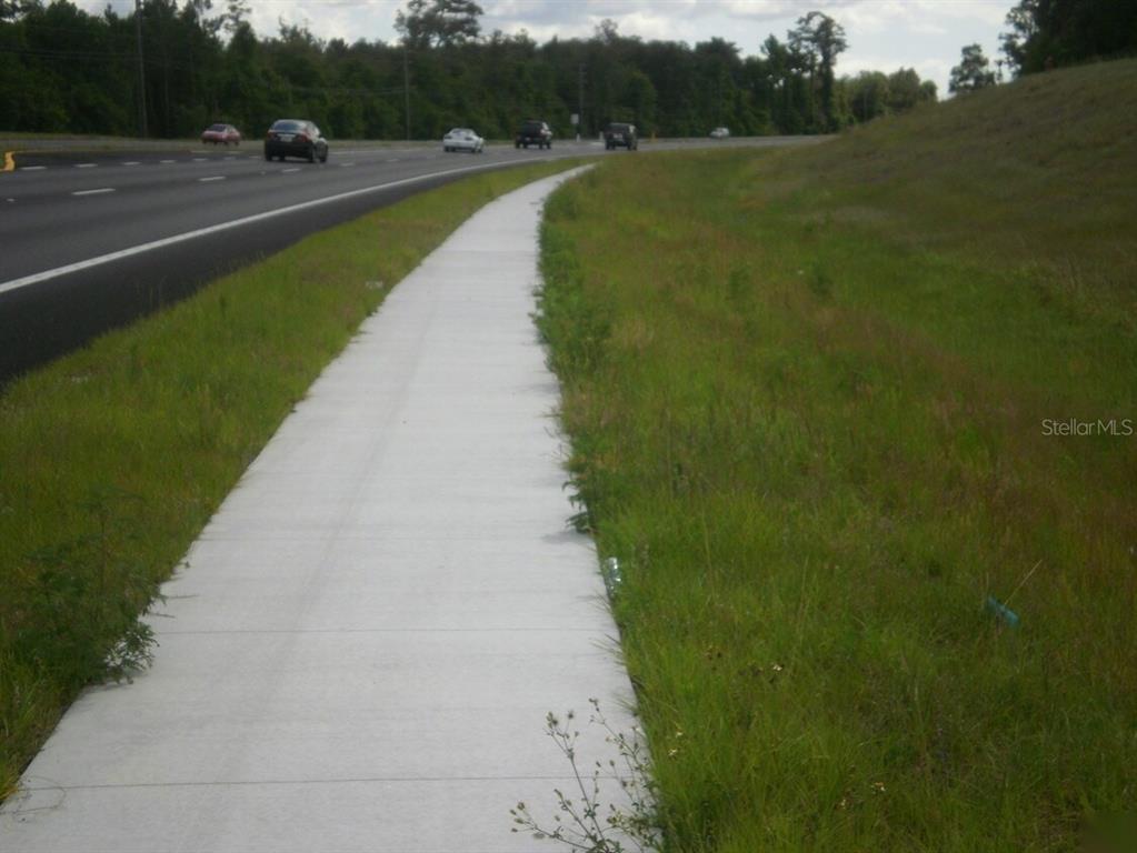 A concrete sidewalk runs alongside a grassy embankment next to a multi-lane highway — TBD CORTEZ BOULEVARD, BROOKSVILLE, FL