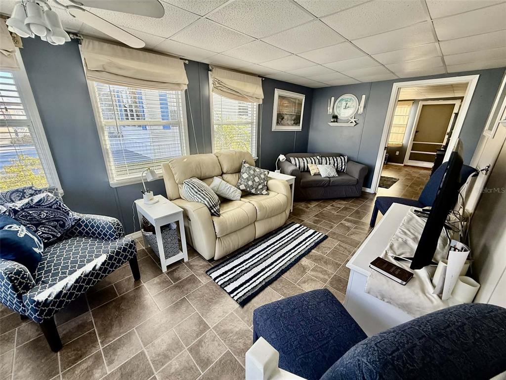 A living room features tile flooring, a beige loveseat, a patterned armchair, and blue walls — 7041 FAIRVIEW VILLAGE CIRCLE, WINTER HAVEN, FL