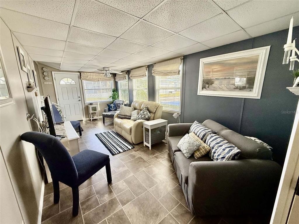 A living room features a gray sofa, a beige loveseat, tile flooring, and a drop ceiling — 7041 FAIRVIEW VILLAGE CIRCLE, WINTER HAVEN, FL