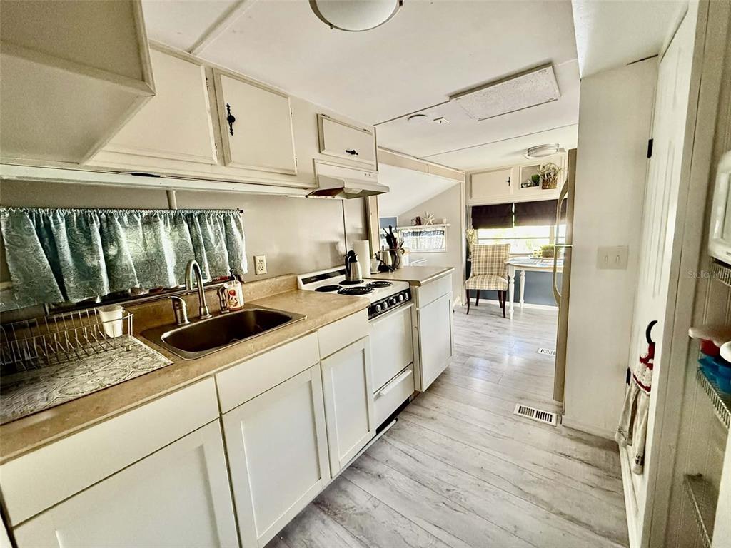 A kitchen features white cabinets, a stainless steel sink, and light wood-look flooring — 7041 FAIRVIEW VILLAGE CIRCLE, WINTER HAVEN, FL