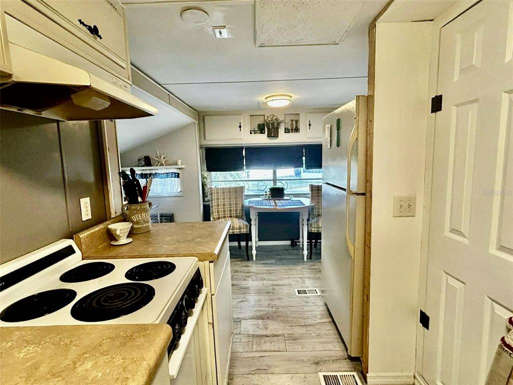 A kitchen with white appliances, wood-look flooring, and a dining area in the background — 7041 FAIRVIEW VILLAGE CIRCLE, WINTER HAVEN, FL