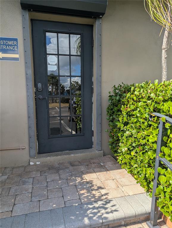 A black glass-paneled door with a keypad lock sits beside a green hedge — 4456 TAMIAMI TRAIL, PUNTA GORDA, FL