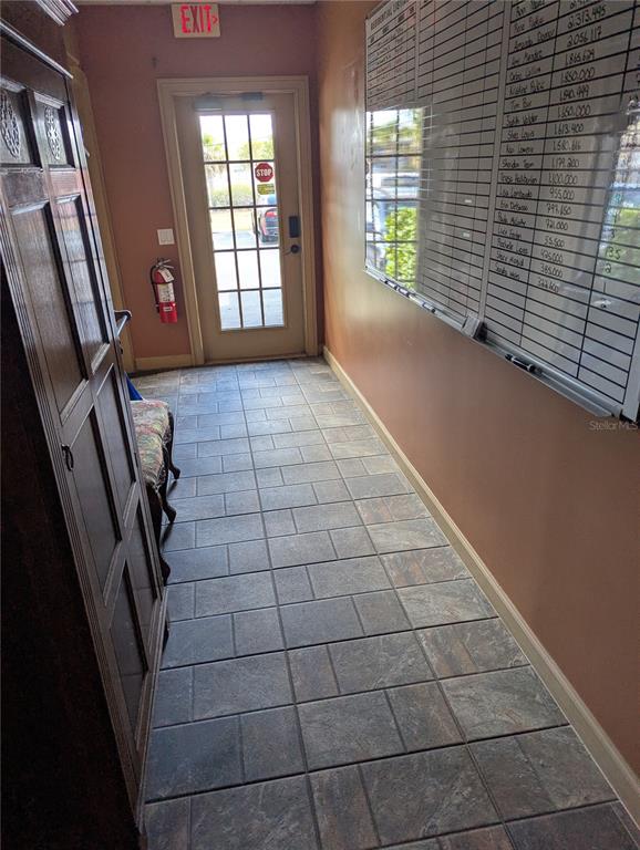 A hallway features tiled flooring, a wooden cabinet, a wall-mounted whiteboard, and an exit door — 4456 TAMIAMI TRAIL, PUNTA GORDA, FL