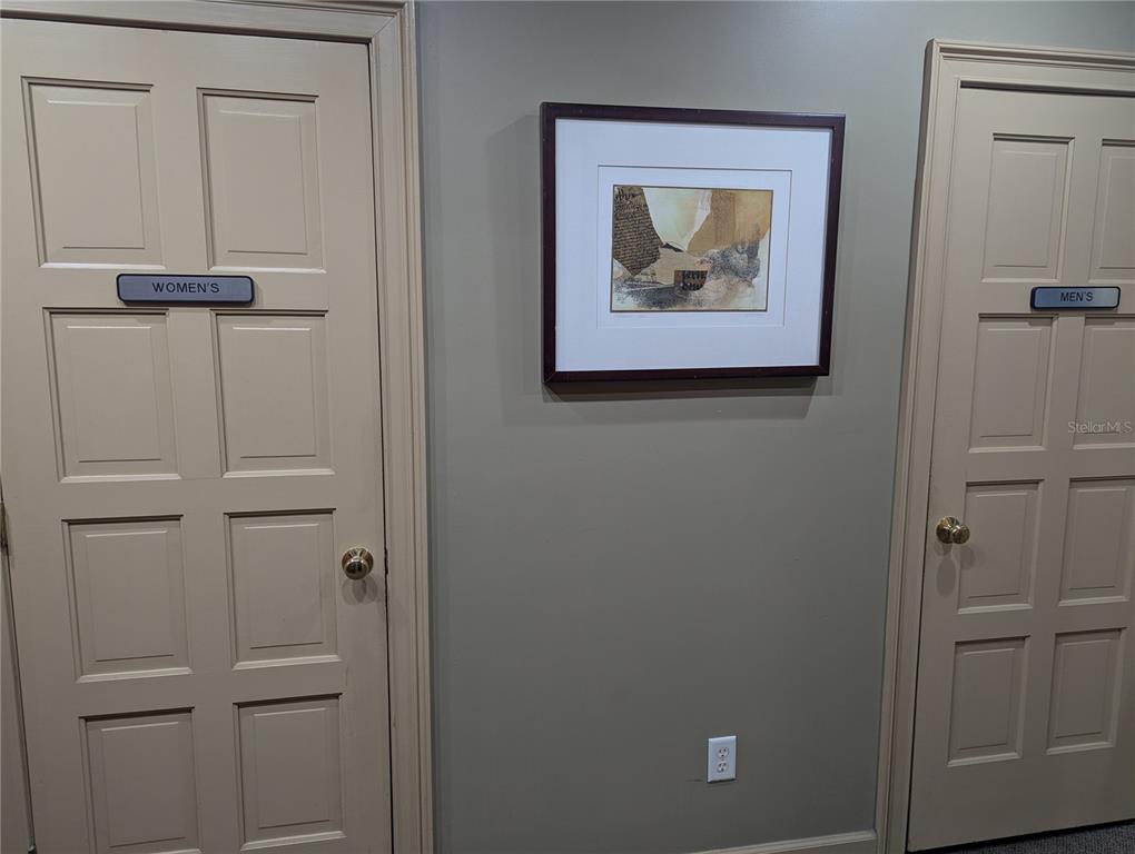 Two beige doors labeled Women's and Men's flank a framed piece of wall art — 4456 TAMIAMI TRAIL, PUNTA GORDA, FL