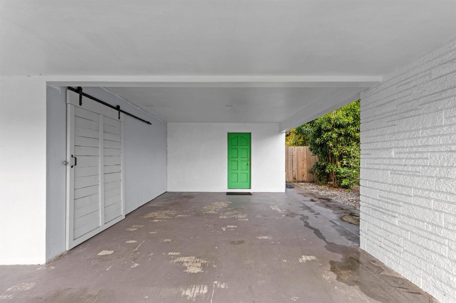 A covered carport features a green door, white walls, and a sliding barn-style door — 2861 SW 9th Street, Boynton Beach FL 33435, BOYNTON BEACH, FL
