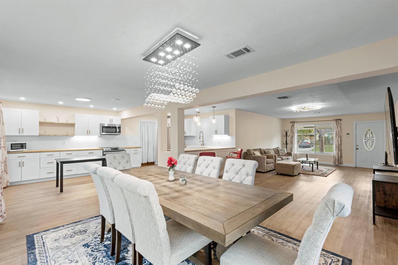 An open-concept dining and living area features a crystal chandelier, white cabinetry, and wood-look flooring — 2861 SW 9th Street, Boynton Beach FL 33435, BOYNTON BEACH, FL