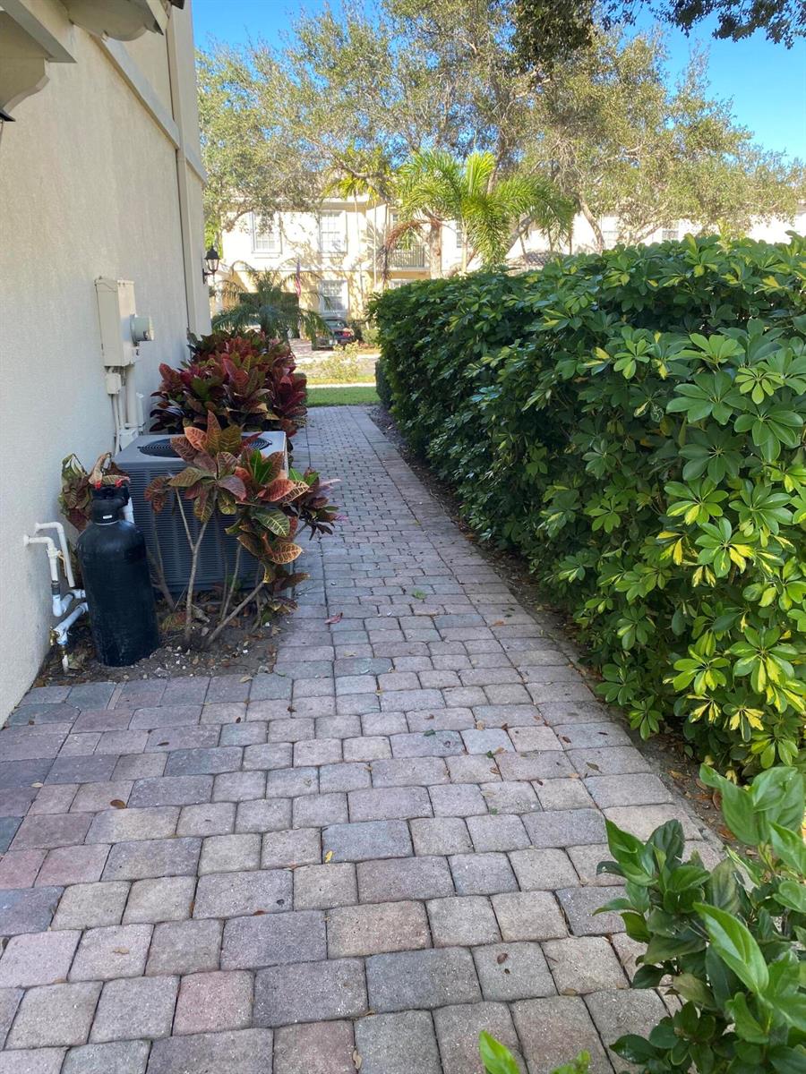 A paved walkway leads past an air conditioning unit and landscaping alongside a building exterior — 477 Capistrano Drive, Palm Beach Gardens FL 33410, PALM BEACH GARDENS, FL