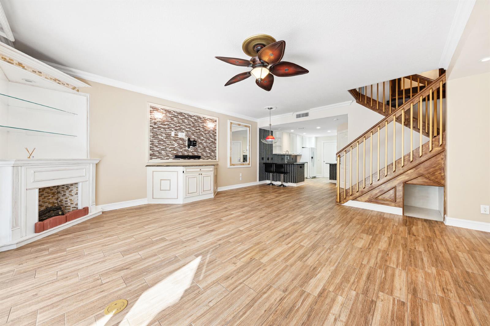 A living room features wood-look tile flooring, a fireplace, a staircase, and an open kitchen — 477 Capistrano Drive, Palm Beach Gardens FL 33410, PALM BEACH GARDENS, FL