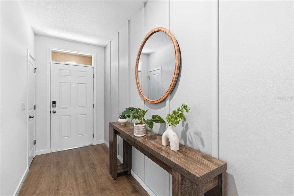 A modern entryway features wood-look flooring, a console table, a round mirror, and board-and-batten walls — 1041 CHAMPION RDG DRIVE, DAYTONA BEACH, FL
