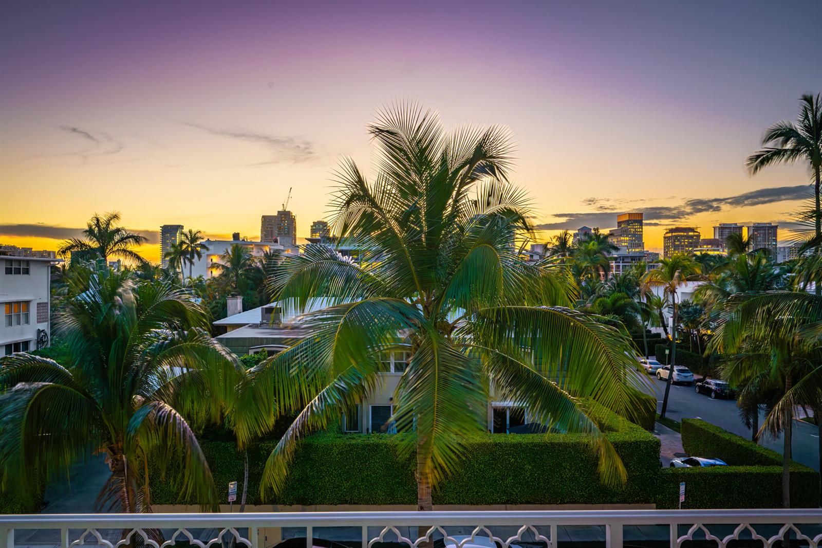 A balcony view overlooks palm trees, a residential street, and a city skyline at sunset — 354 Chilean Avenue # 4d, Palm Beach FL 33480, PALM BEACH, FL