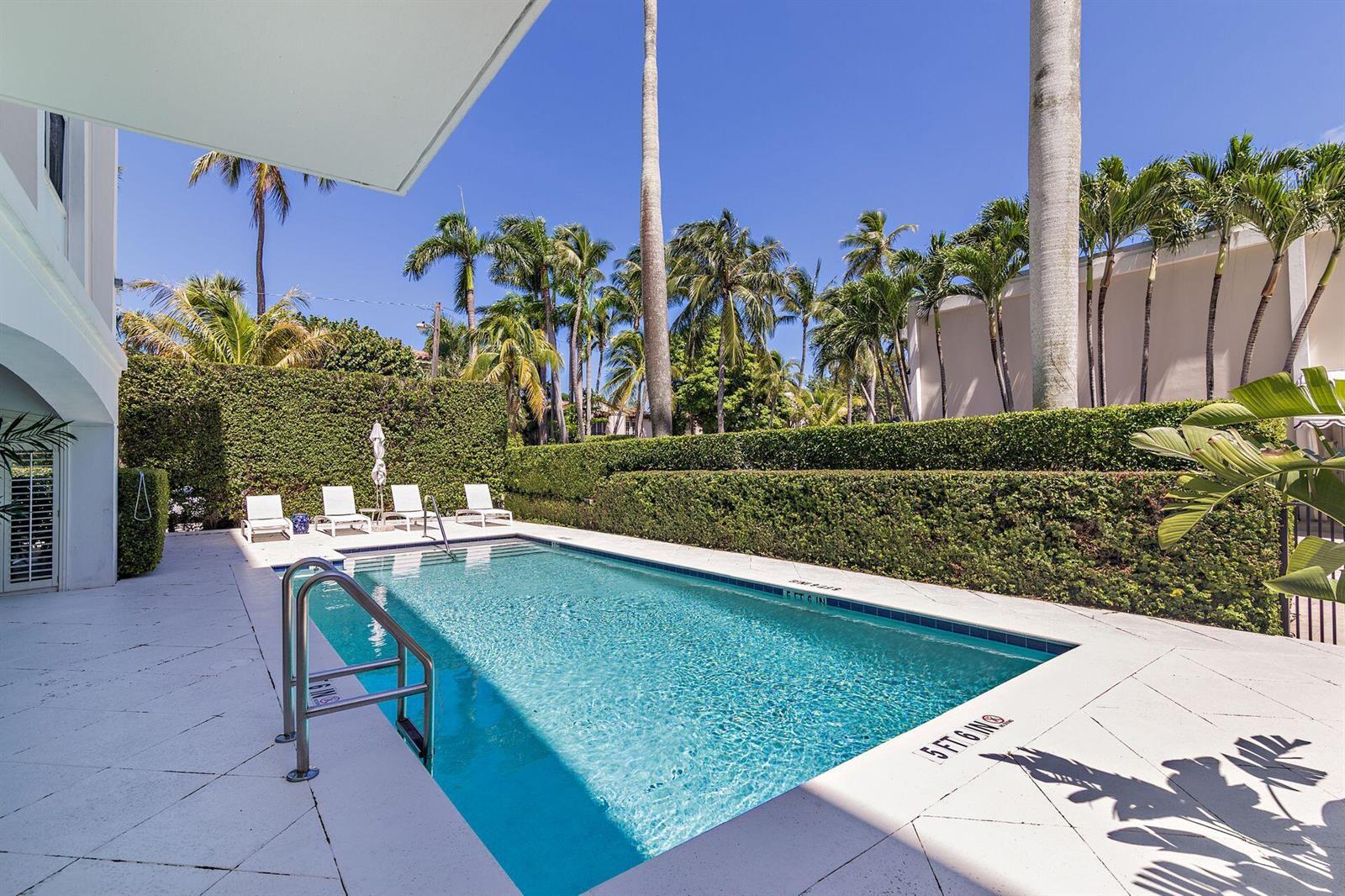 A rectangular swimming pool with a metal ladder sits on a patio beside palm trees — 354 Chilean Avenue # 4d, Palm Beach FL 33480, PALM BEACH, FL