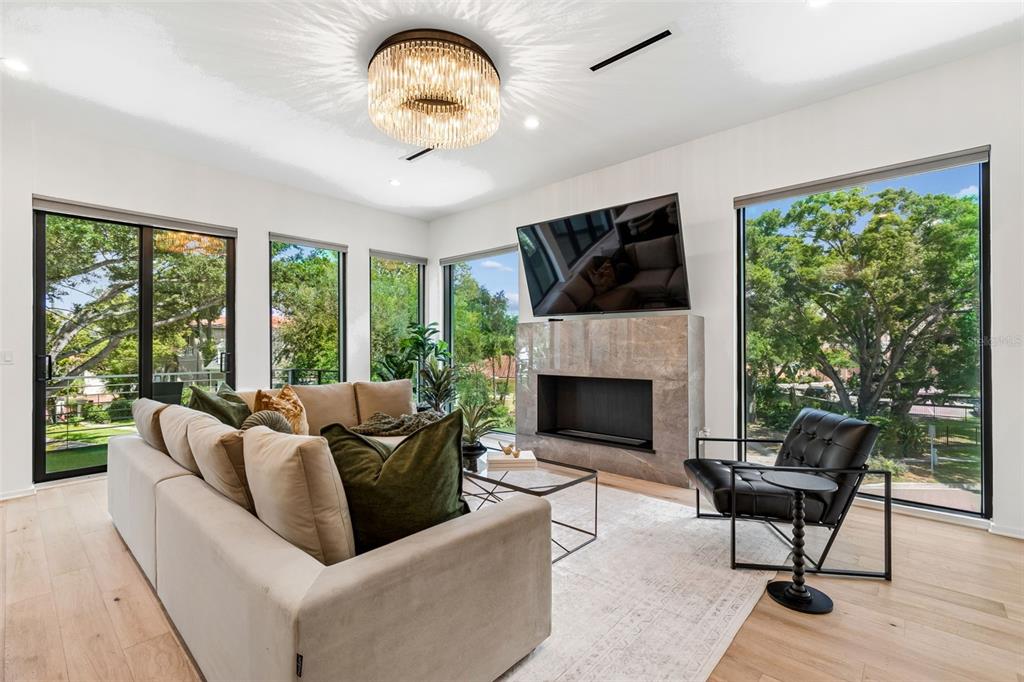 A modern living room features a fireplace, large windows, a sofa, and a crystal chandelier — 94 W DAVIS BLVD., TAMPA, FL