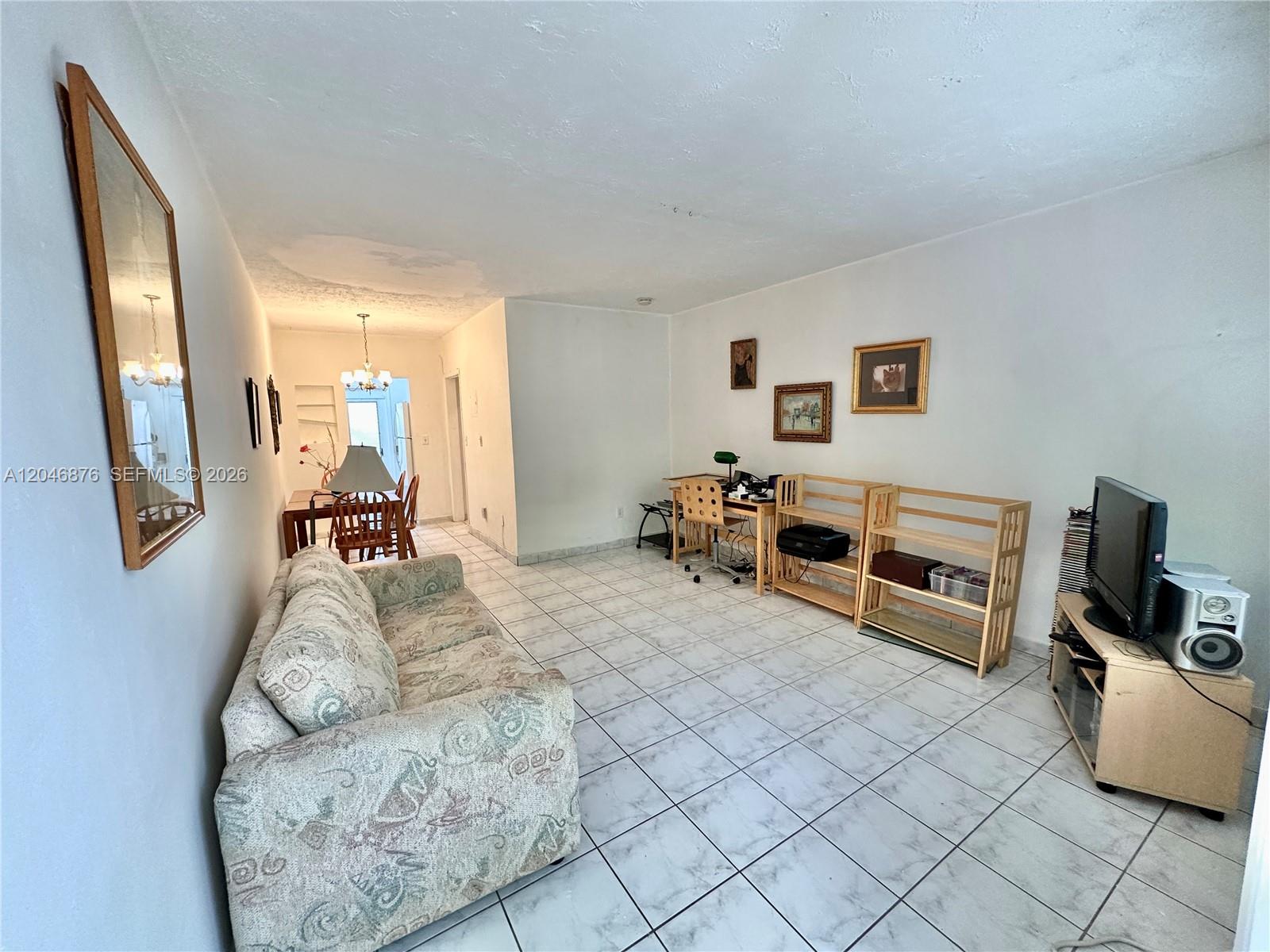 A living room features a patterned sofa, tile flooring, and a dining area beyond — 8132 Harding Ave # 6, Miami Beach FL 33141, MIAMI BEACH, FL