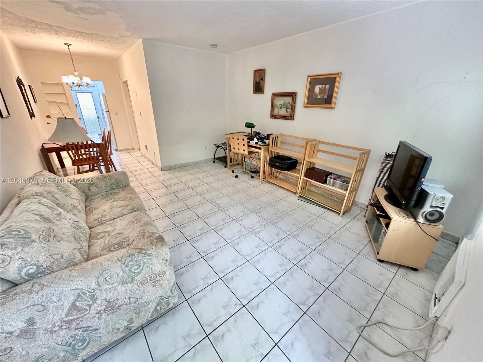 A living room with white tile floors, a patterned sofa, wooden shelving, and a television — 8132 Harding Ave # 6, Miami Beach FL 33141, MIAMI BEACH, FL