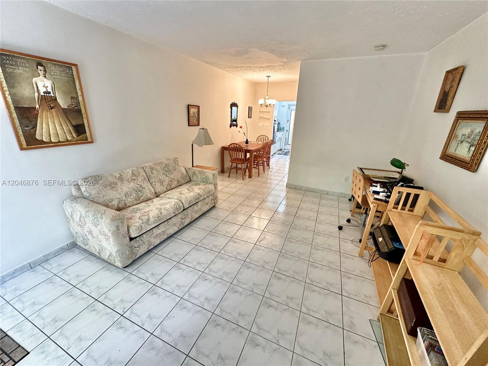 A living room with tile floors, a patterned sofa, a dining area, and a desk — 8132 Harding Ave # 6, Miami Beach FL 33141, MIAMI BEACH, FL