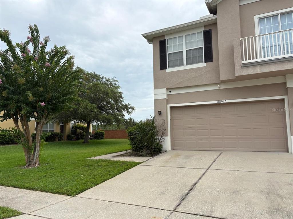 A two-story house exterior features a beige stucco facade, a tan garage door, and a balcony — 10907 DERRINGER DRIVE, ORLANDO, FL