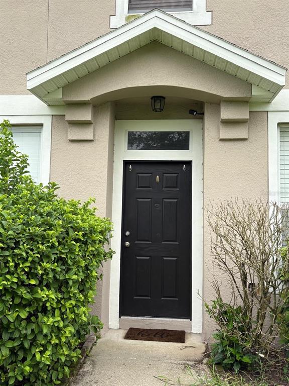 A black front door is centered under a gabled porch roof with beige stucco siding — 10907 DERRINGER DRIVE, ORLANDO, FL