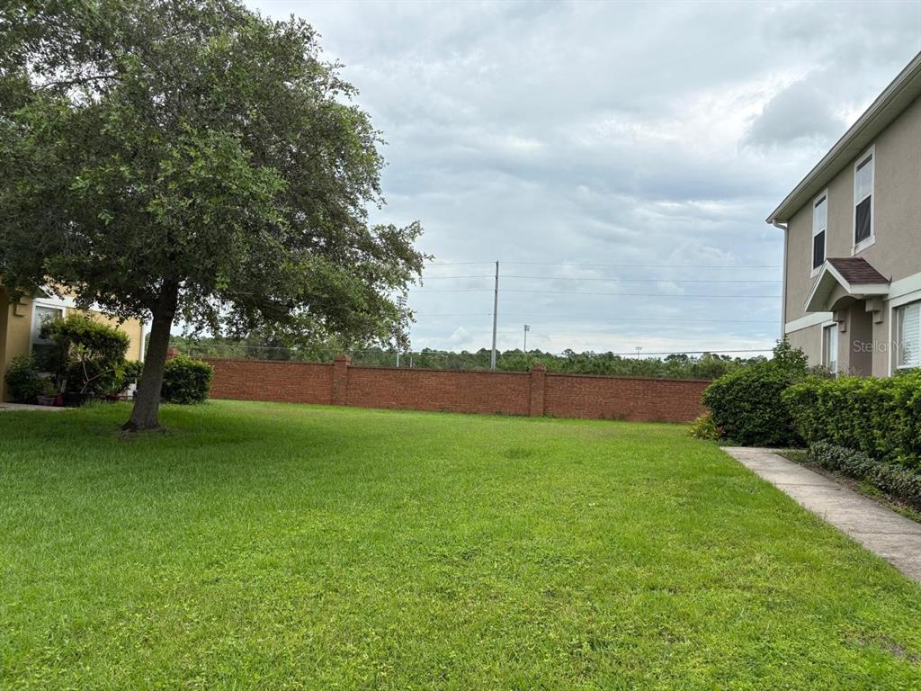 A grassy backyard features a large tree, a brick wall, and a multi-story building — 10907 DERRINGER DRIVE, ORLANDO, FL