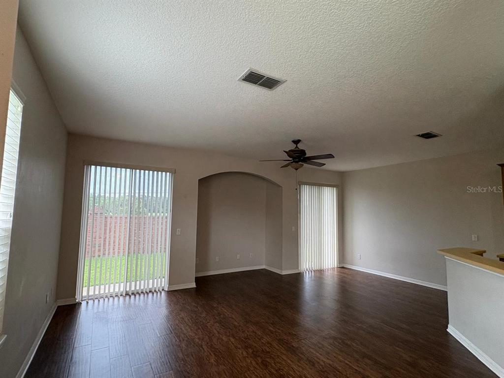 An empty living room features dark wood-look flooring, an arched wall niche, and vertical blinds — 10907 DERRINGER DRIVE, ORLANDO, FL