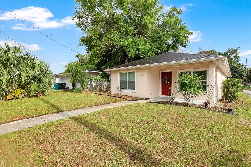 A single-story house with light-colored stucco walls, a red front door, and a grassy yard — 3936 THOMAS STREET, ORLANDO, FL