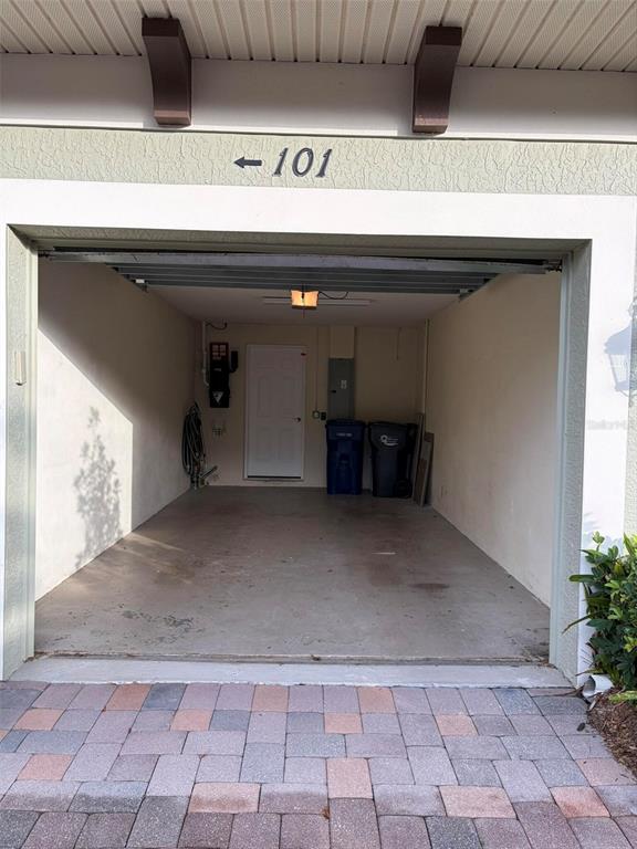 An open garage with a concrete floor, a white door, and two trash bins inside — 6536 MOORINGS POINT CIRCLE UNIT 101, LAKEWOOD RANCH, FL