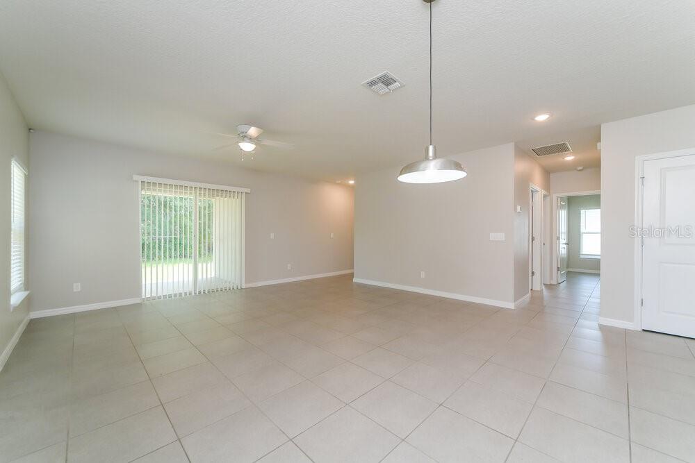 A bright, open-concept living area features light tile flooring, a ceiling fan, and sliding glass doors — 1201 CROYDON CIRCLE, KISSIMMEE, FL