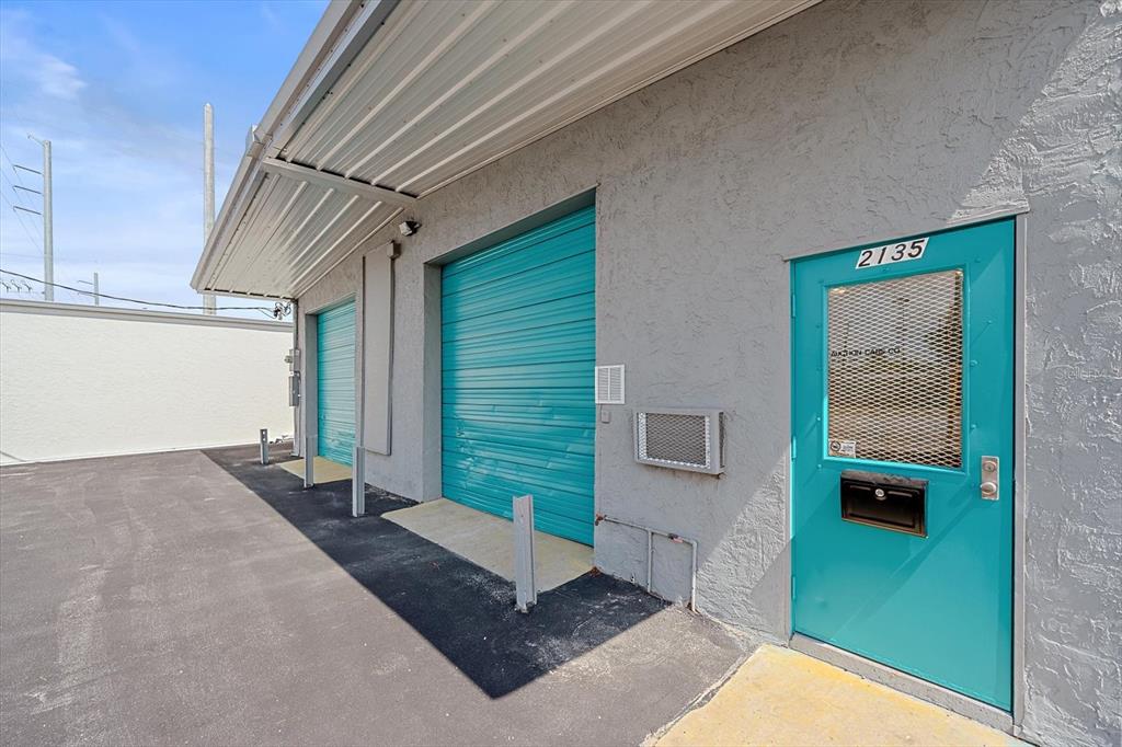 An exterior view of a commercial building with two teal roll-up doors and a door — 2135 12TH STREET, SARASOTA, FL