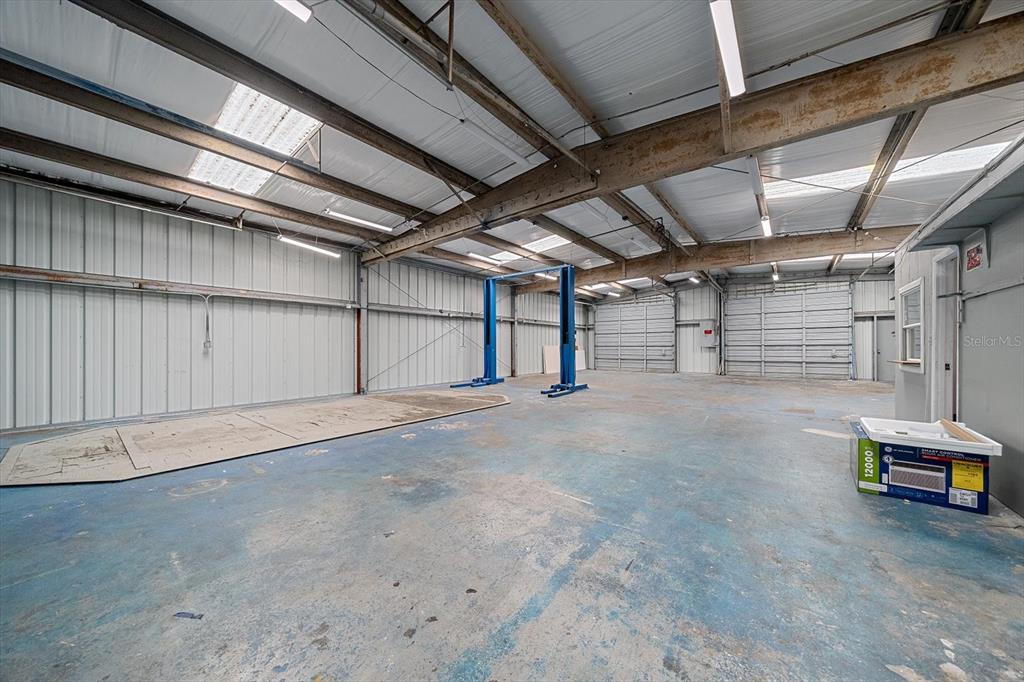 An industrial warehouse space features a blue vehicle lift, concrete floors, and metal walls — 2135 12TH STREET, SARASOTA, FL