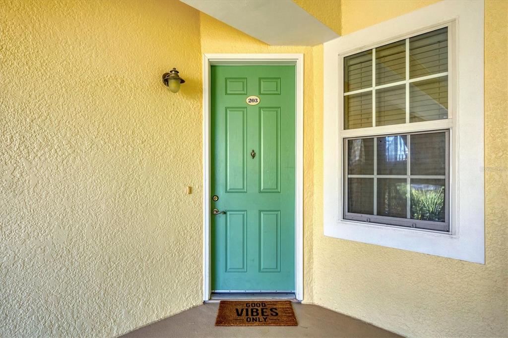 A green front door with the number 203 sits on a yellow stucco exterior wall — 8541 AMBERJACK CIRCLE UNIT 203, ENGLEWOOD, FL