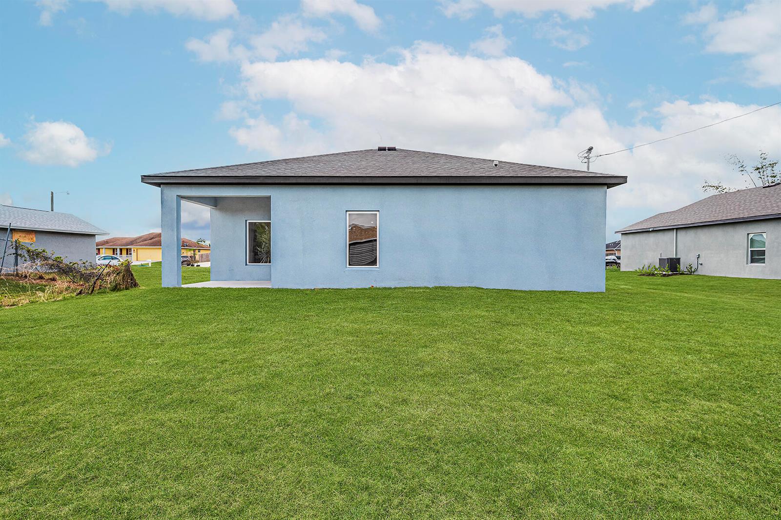 The rear exterior of a light blue single-story house features a covered patio and lawn — 8585 101st Avenue, Vero Beach FL 32967, VERO BEACH, FL