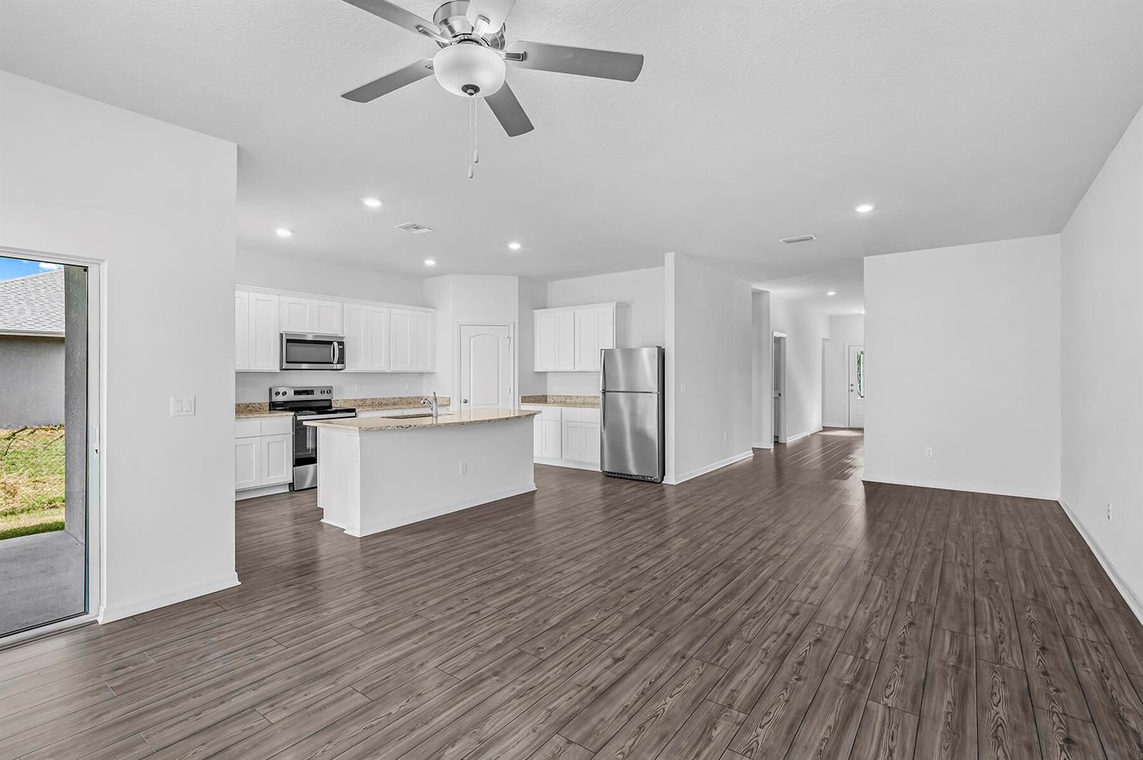 A kitchen with white cabinets, granite countertops, and stainless steel appliances opens to a living area — 8585 101st Avenue, Vero Beach FL 32967, VERO BEACH, FL