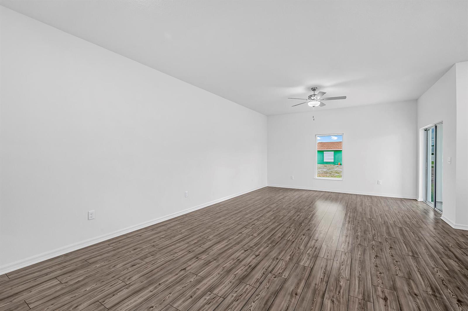 An empty living room features white walls, wood-look flooring, a ceiling fan, and sliding doors — 8585 101st Avenue, Vero Beach FL 32967, VERO BEACH, FL