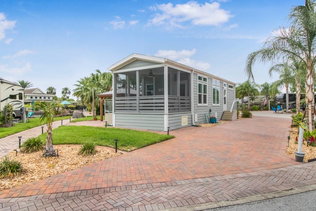 A light green manufactured home with a screened-in porch sits on a paved brick lot — 6820 AMANDA VISTA CIRCLE, LAND O LAKES, FL