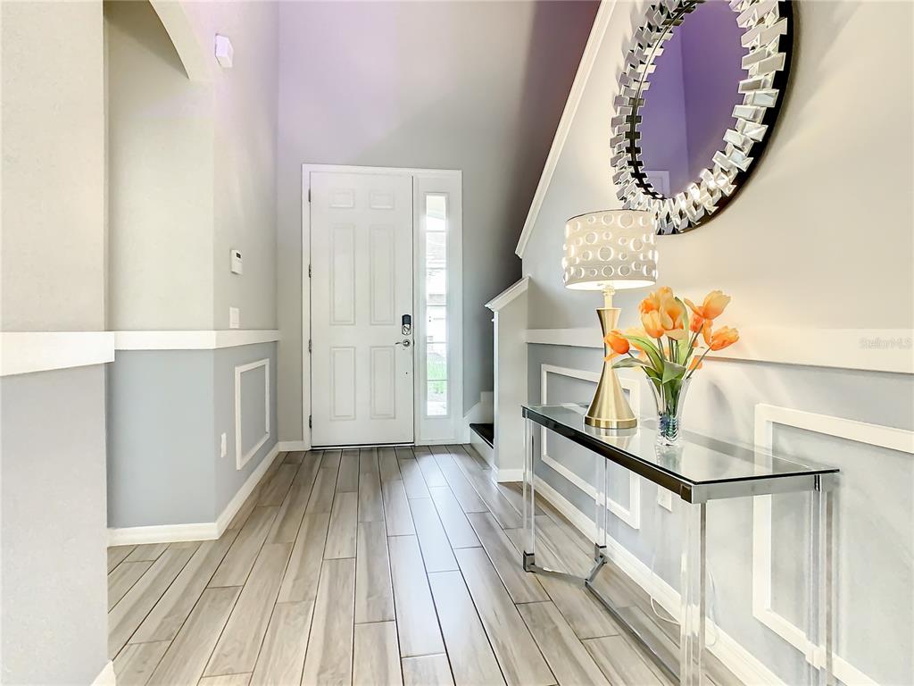 A bright entryway features light wood-look tile flooring, a glass console table, and a round mirror — 6121 BROAD OAK DRIVE, DAVENPORT, FL