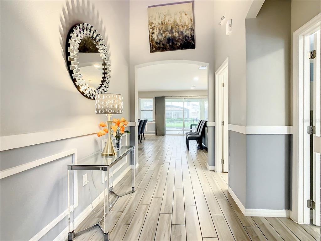 A bright entryway features a glass console table, a round mirror, and wood-look tile flooring — 6121 BROAD OAK DRIVE, DAVENPORT, FL