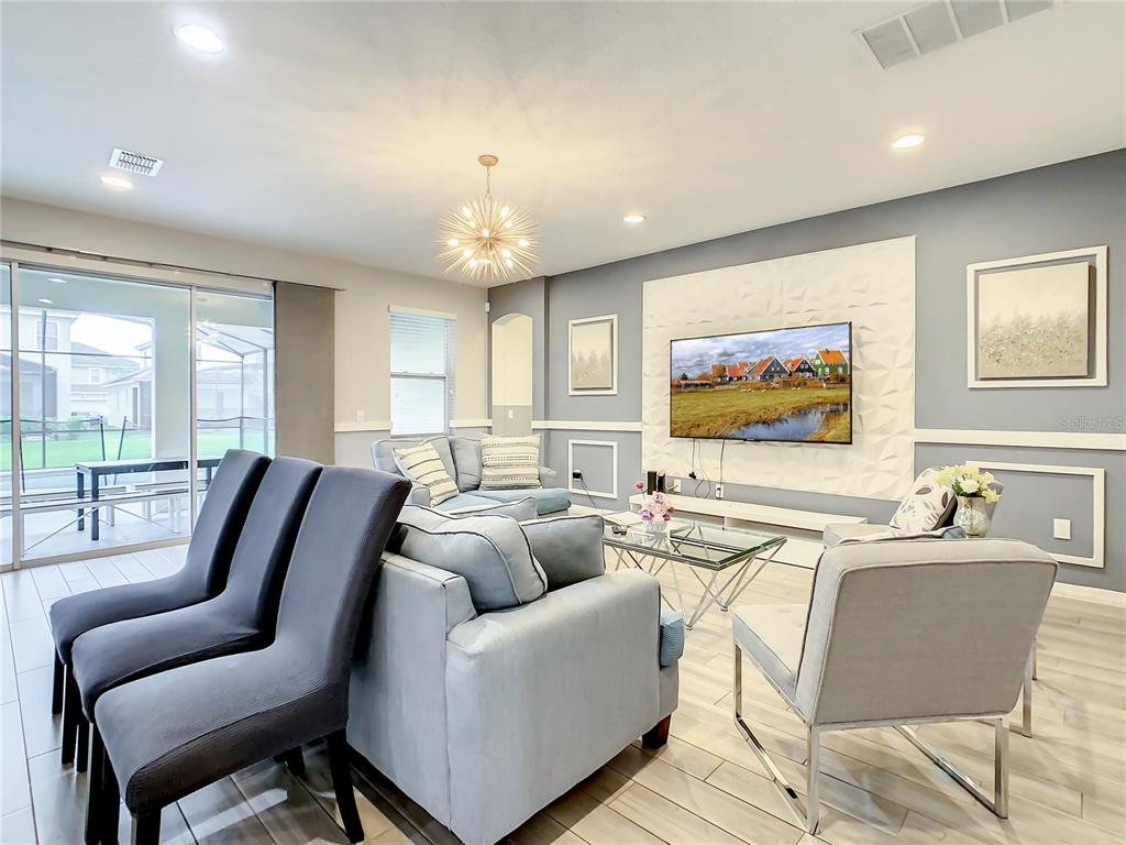 A living room features a textured accent wall with a television, light blue furniture, and tile flooring — 6121 BROAD OAK DRIVE, DAVENPORT, FL