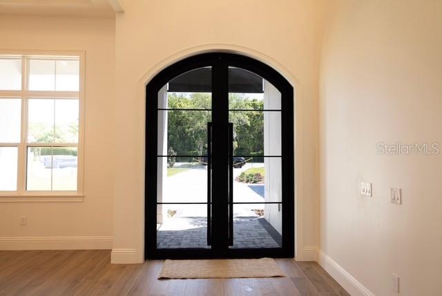 An arched black-framed glass double door opens to an outdoor patio with light wood flooring — 26112 ESTATES RIDGE DRIVE, SORRENTO, FL