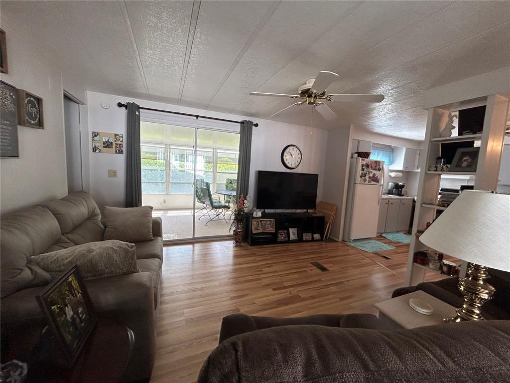 A living room with wood-look flooring, a ceiling fan, and sliding doors to a patio — 131 MALAYON WAY, LEESBURG, FL