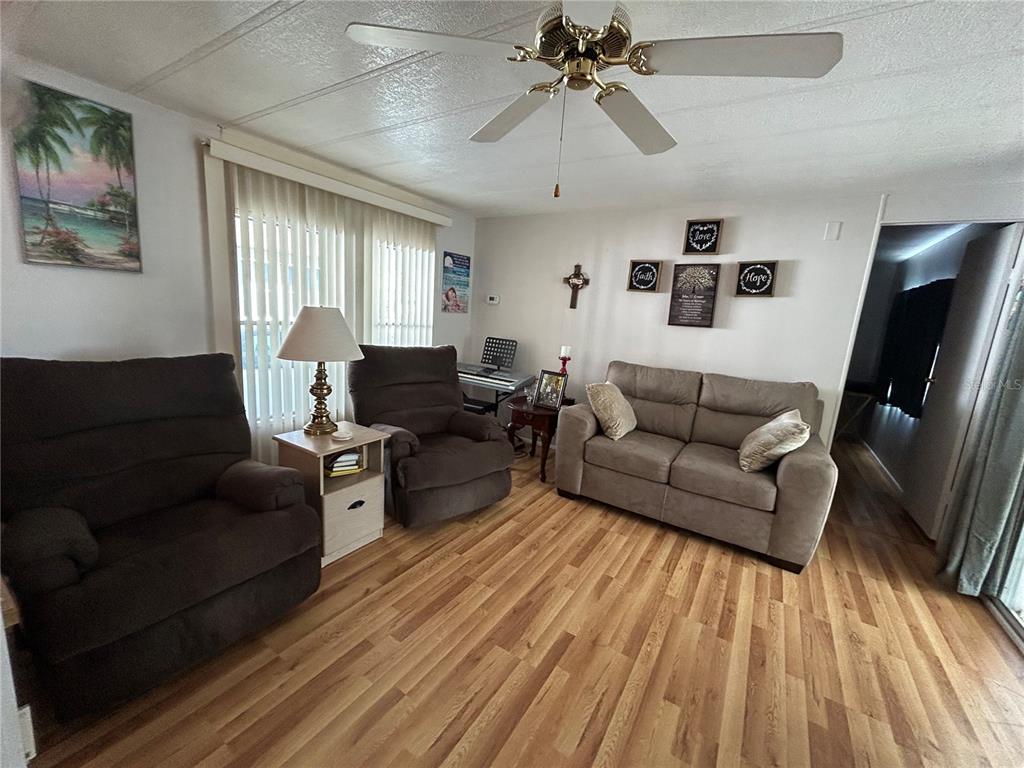 A living room features wood-look flooring, a ceiling fan, and brown upholstered furniture — 131 MALAYON WAY, LEESBURG, FL