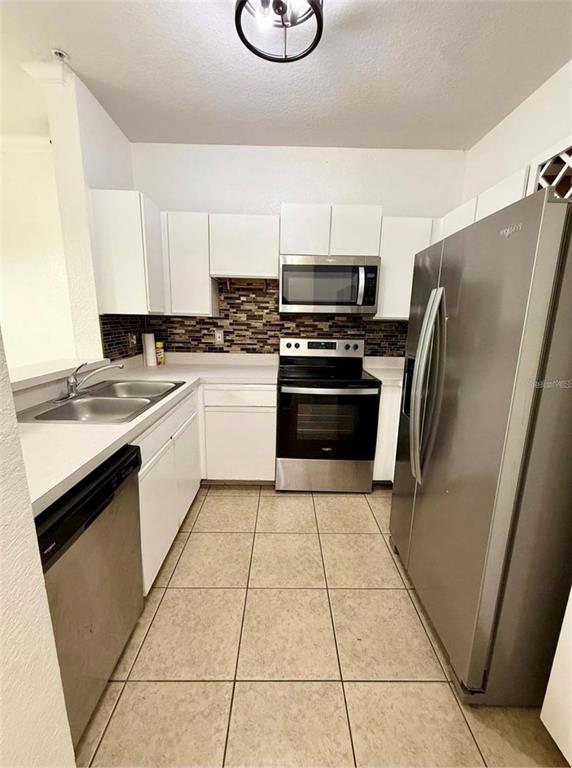 A kitchen features white cabinets, stainless steel appliances, a tiled backsplash, and light floor tiles — 2674 ROBERT TRENT JONES DRIVE UNIT 337, ORLANDO, FL